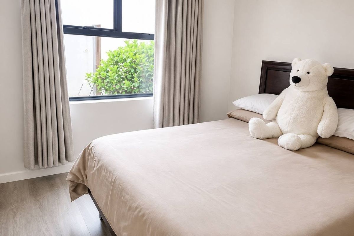 A well-maintained bedroom featuring neutral walls, laminate flooring, and a large window with integrated curtain tracks.