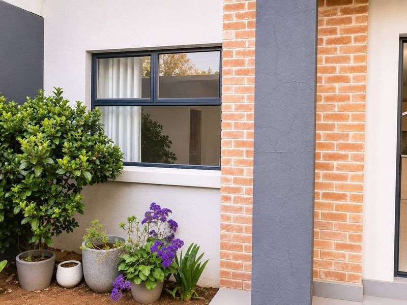 A view of a rear patio area featuring a brick and painted facade, leading into a modern open-plan kitchen interior.
