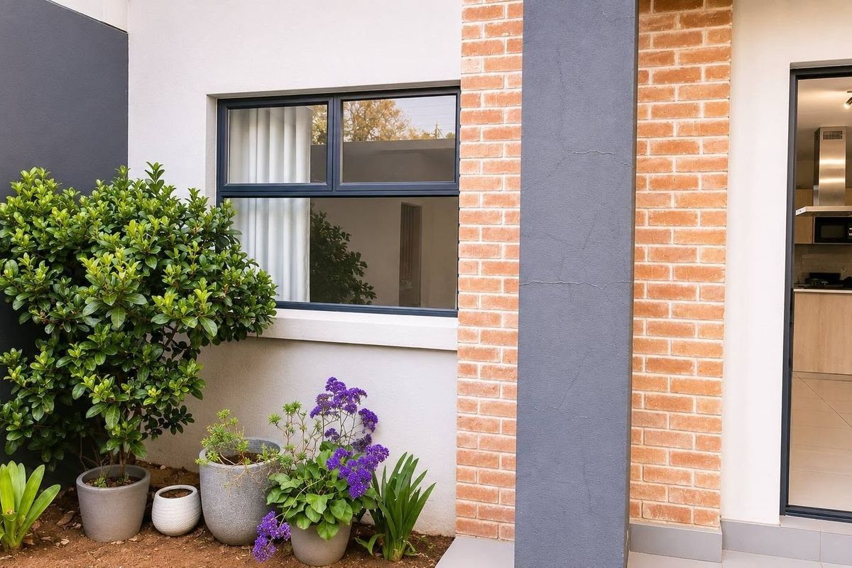 A view of a rear patio area featuring a brick and painted facade, leading into a modern open-plan kitchen interior.