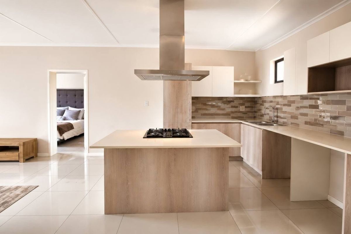 Modern kitchen featuring a central island with a gas hob, stainless steel extractor, stone countertops, and sleek cabinetry with a subway tile backsplash.