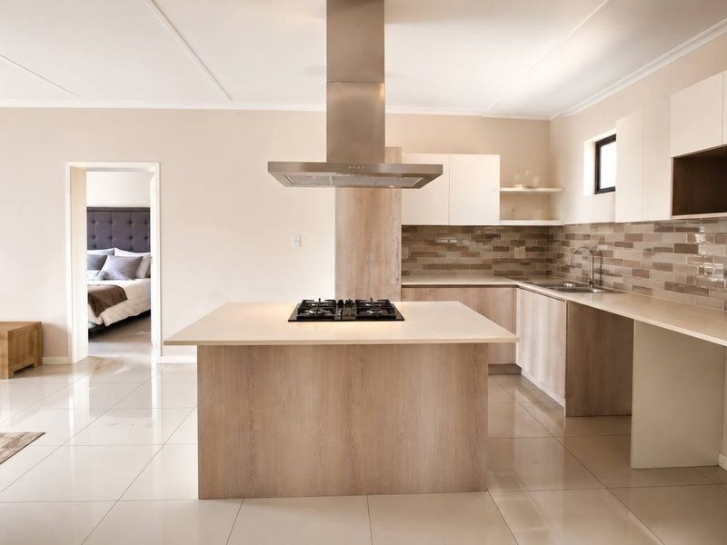 Modern kitchen featuring a central island with a gas hob, stainless steel extractor, stone countertops, and sleek cabinetry with a subway tile backsplash.