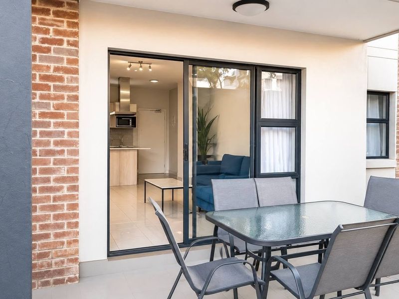 A covered patio area featuring tiled flooring and exposed brick accents, providing seamless access to the interior living space through sliding glass doors.