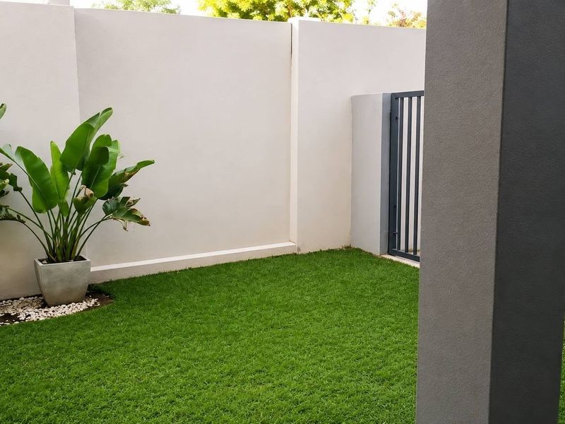 A well-maintained private garden area featuring artificial turf, high boundary walls for privacy, and a secure metal gate.