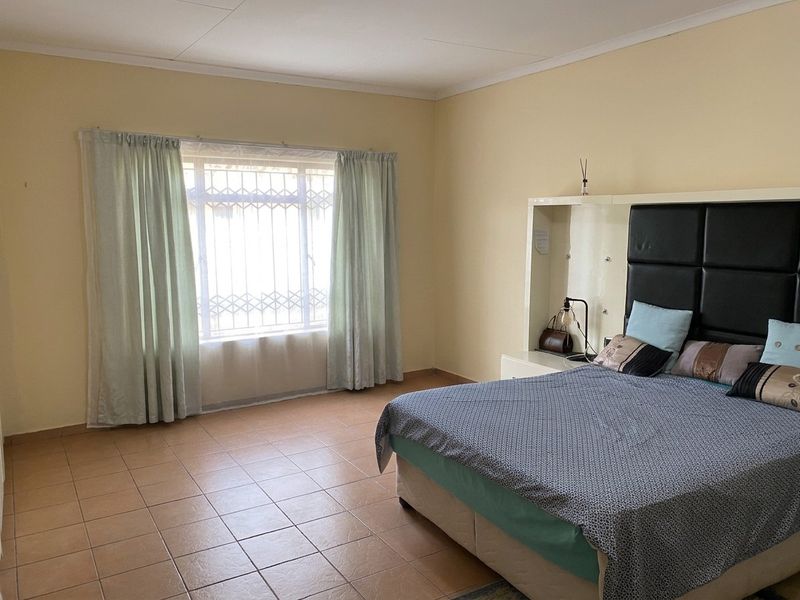 A spacious bedroom featuring tiled flooring, a built-in headboard unit, and a window fitted with a security gate.