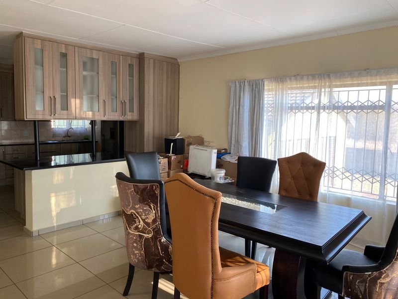 Open plan kitchen and dining area featuring modern wood-finish cabinetry, granite countertops, tiled flooring, and large windows with security gates.