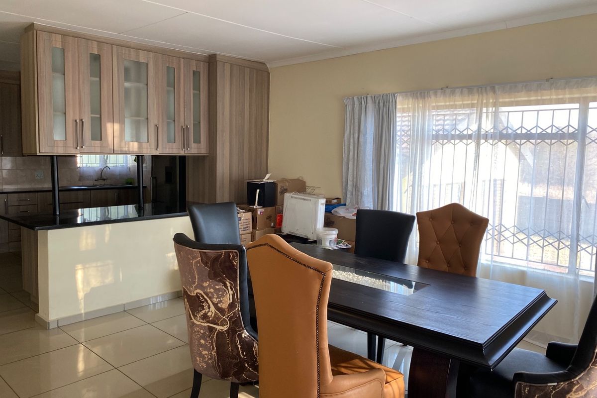 Open plan kitchen and dining area featuring modern wood-finish cabinetry, granite countertops, tiled flooring, and large windows with security gates.