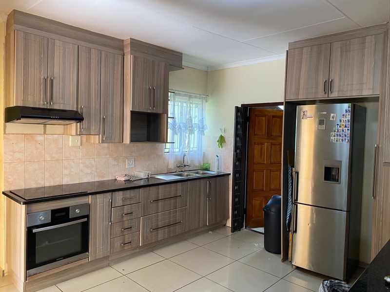 A functional kitchen featuring wood-look cabinetry, dark countertops, built-in oven, extractor fan, and tiled flooring with direct access to an exterior door.