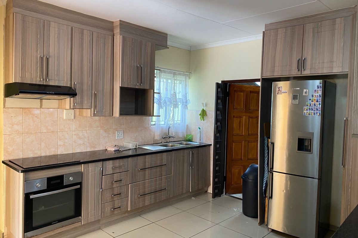 A functional kitchen featuring wood-look cabinetry, dark countertops, built-in oven, extractor fan, and tiled flooring with direct access to an exterior door.