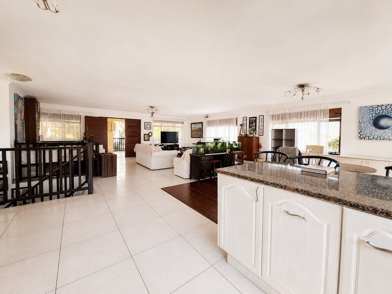 Spacious open-plan living area featuring a granite-topped kitchen island, tiled flooring, and a staircase with a wooden balustrade leading to the lower level.