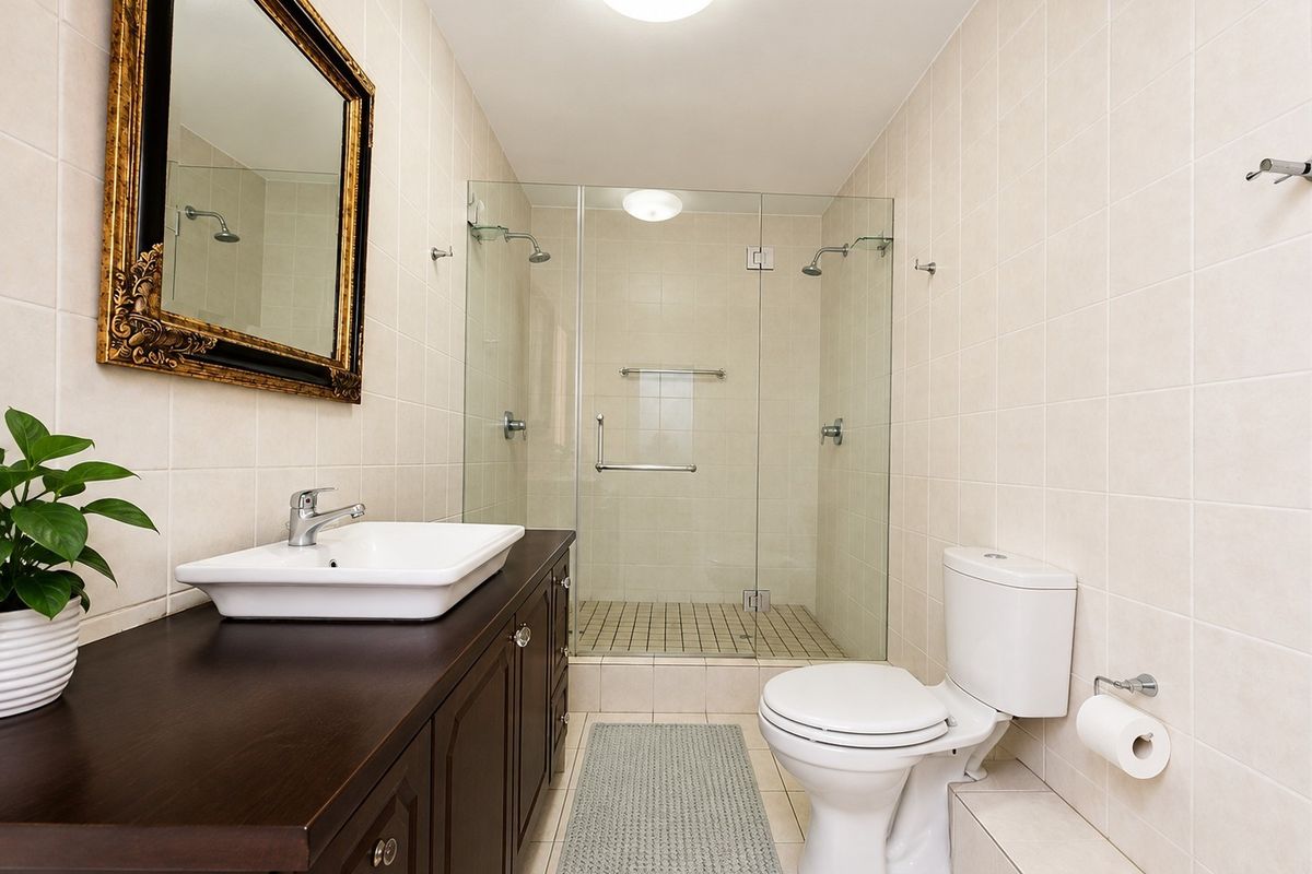 A well-maintained bathroom featuring a dark wood vanity with a vessel sink, a glass-enclosed shower, and neutral wall tiling.
