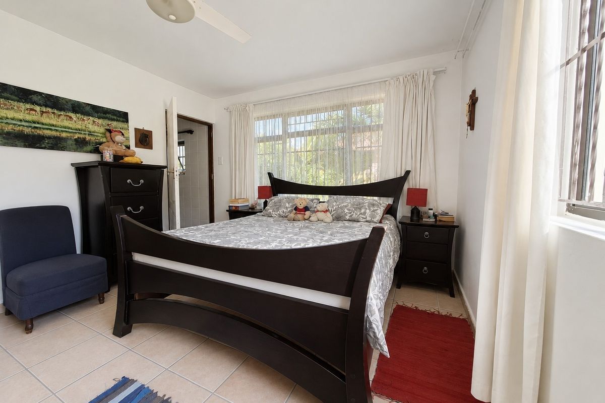 A bedroom featuring tiled flooring, a ceiling fan, and large windows with security bars, providing natural light and access to an en-suite bathroom.