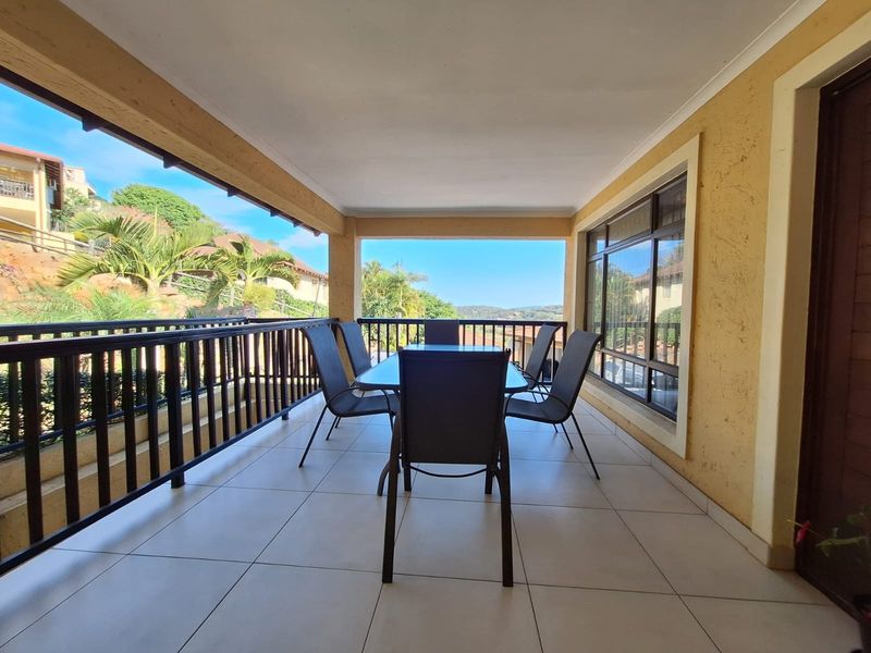 A spacious covered balcony featuring tiled flooring and a metal balustrade, offering an open-air dining space with scenic views.
