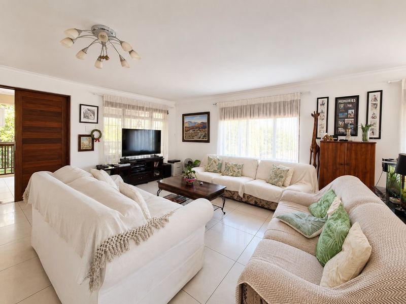 A bright and spacious living room featuring neutral tiled flooring, large windows with natural light, and direct access to an outdoor area via a sliding door.