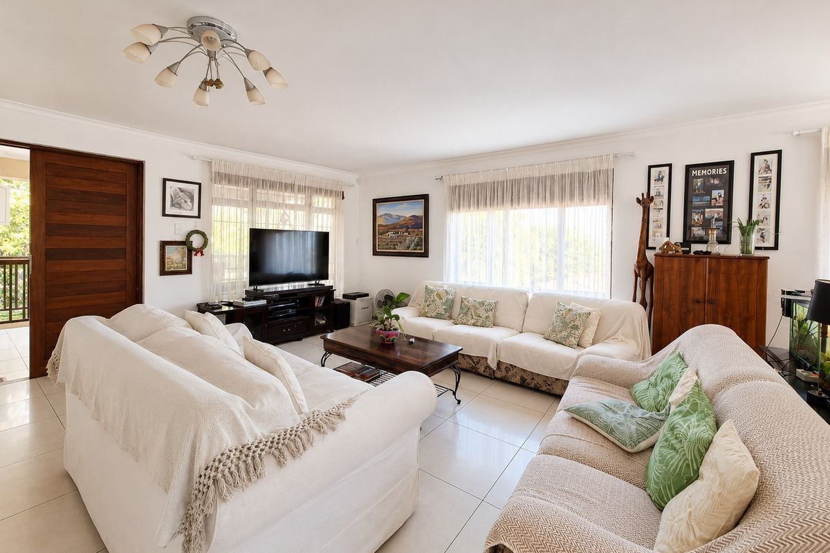 A bright and spacious living room featuring neutral tiled flooring, large windows with natural light, and direct access to an outdoor area via a sliding door.