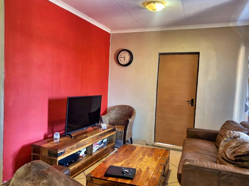 A living room featuring tiled flooring, a bold red accent wall, and a standard internal door, requiring minor cosmetic updates to improve the finish.