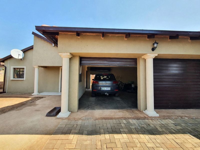 A functional double garage featuring a roll-up door, decorative columns, and exposed rafter eaves, set against a paved driveway area.