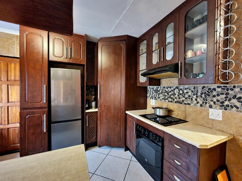 A functional kitchen featuring dark wood cabinetry, stone tile backsplash, integrated electric hob and oven, and tiled flooring.