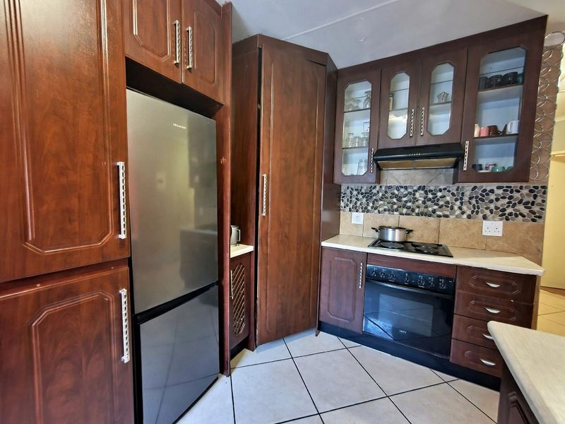 A functional kitchen featuring dark wood cabinetry, a pebble mosaic backsplash, built-in oven, electric hob, and tiled flooring.