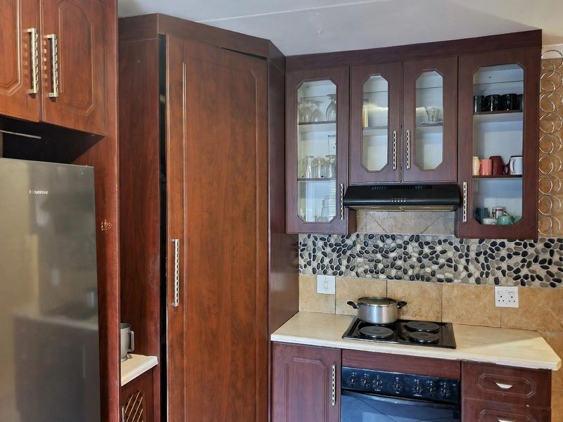 A functional kitchen featuring dark wood cabinetry, a stone pebble mosaic backsplash, built-in oven, and electric hob with an integrated extractor fan.