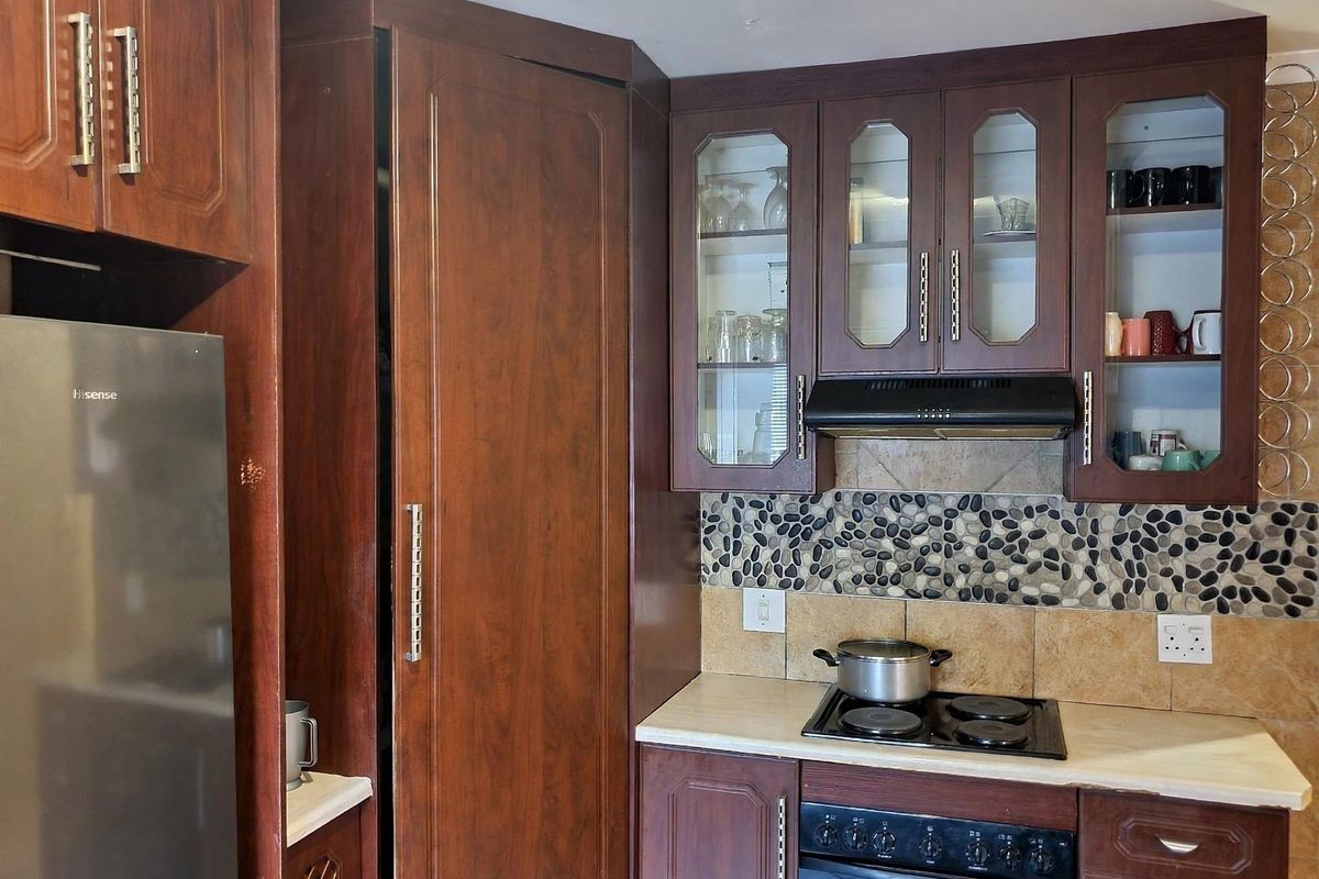 A functional kitchen featuring dark wood cabinetry, a stone pebble mosaic backsplash, built-in oven, and electric hob with an integrated extractor fan.