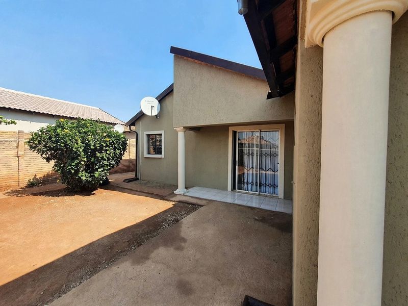 Rear exterior view of the house featuring a tiled patio area, sliding glass door with security gate, and a surrounding garden space.
