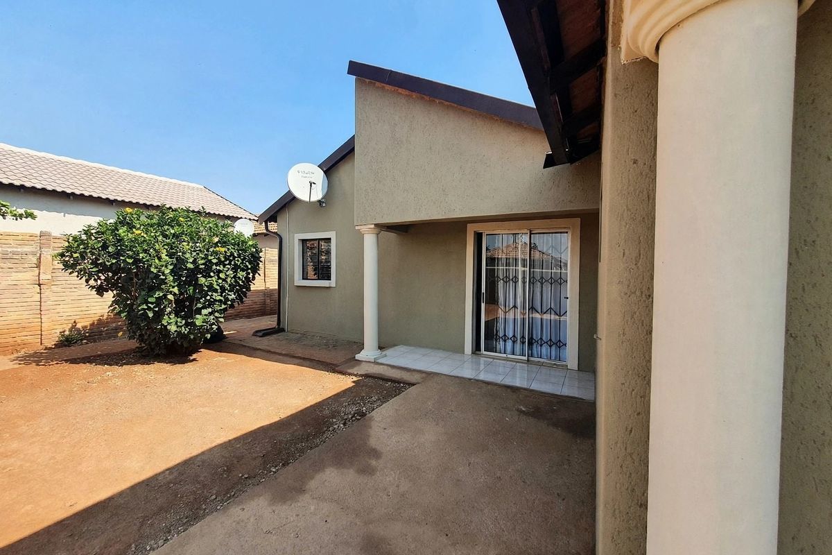 Rear exterior view of the house featuring a tiled patio area, sliding glass door with security gate, and a surrounding garden space.