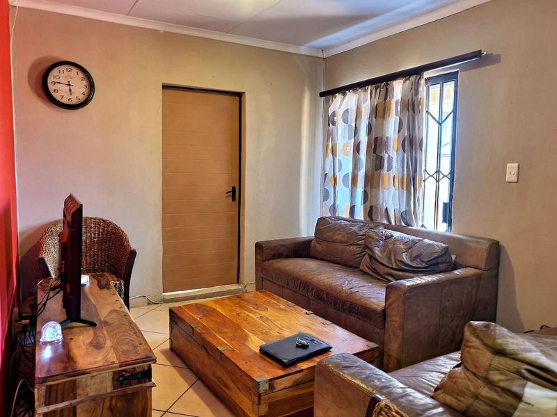 A comfortable living room featuring tiled flooring, a window with security bars, and a neutral wall finish.