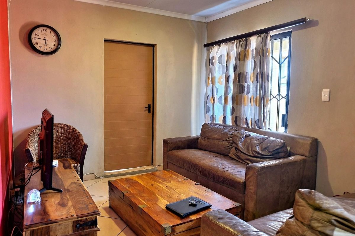 A comfortable living room featuring tiled flooring, a window with security bars, and a neutral wall finish.