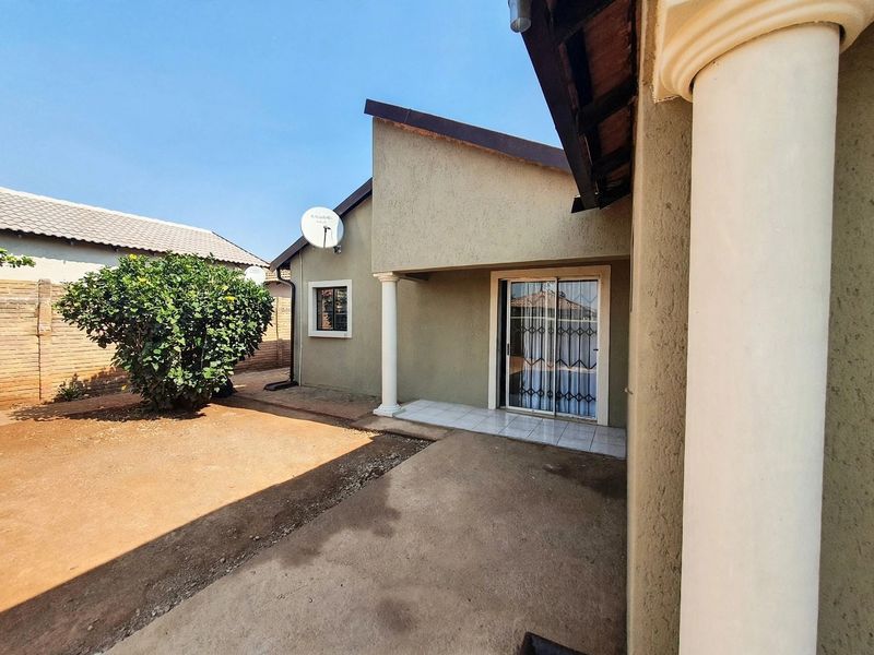 Rear exterior view of the property featuring a tiled patio area, sliding glass door with security gate, and concrete ground surfacing.