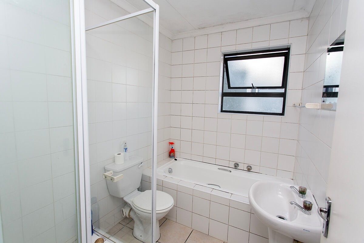 A dated bathroom featuring a shower enclosure, bathtub, pedestal basin, and toilet with white wall tiling and a top-hung window.