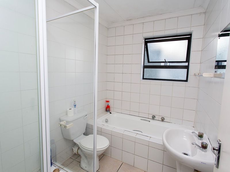 A dated bathroom featuring a shower enclosure, bathtub, pedestal basin, and toilet with white wall tiling and a top-hung window.