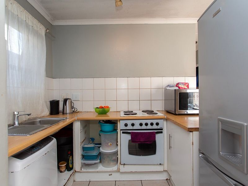 Compact kitchen featuring a built-in oven, electric hob, stainless steel sink, and tiled splashback, requiring some cosmetic updates to cabinetry and finishes.