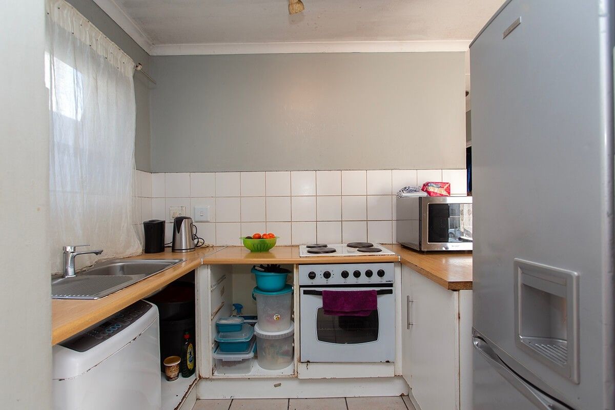 Compact kitchen featuring a built-in oven, electric hob, stainless steel sink, and tiled splashback, requiring some cosmetic updates to cabinetry and finishes.