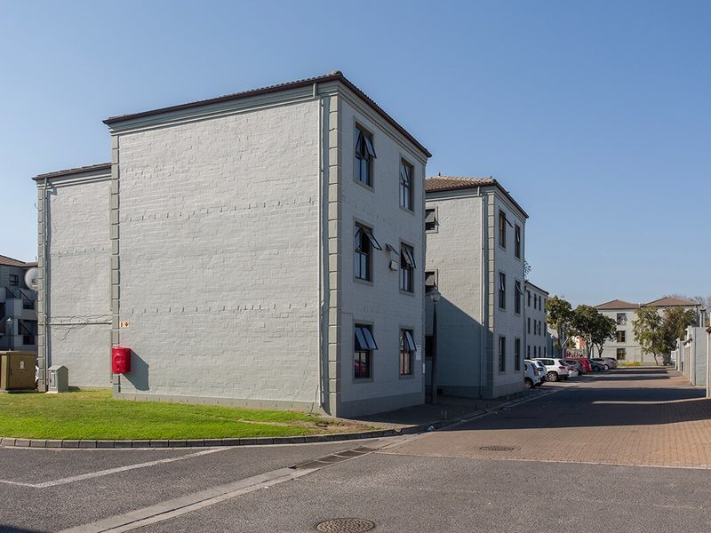 Exterior view of a multi-story apartment complex featuring painted brick facades, tiled roofing, and paved driveway access.