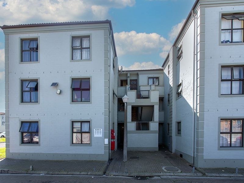Exterior view of a multi-story apartment block featuring a paved courtyard entrance, external stairwell access, and functional security lighting.