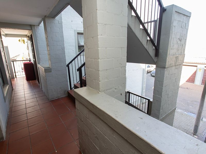 An exterior balcony area featuring tiled flooring, painted brick pillars, and a metal staircase leading to the upper level.