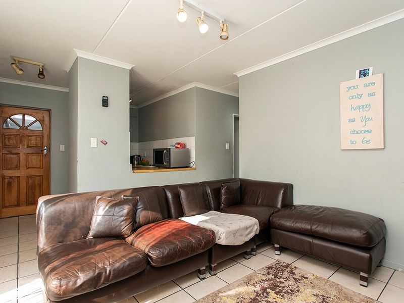 Open plan living area featuring tiled flooring, track lighting, and a convenient kitchen pass-through window, connecting the living space to the kitchen area.