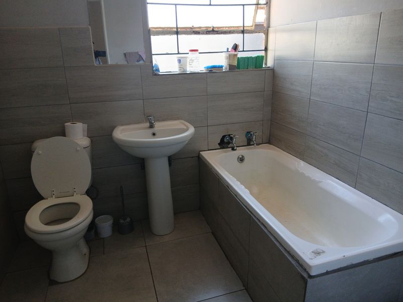 A functional bathroom featuring a pedestal basin, bathtub, and toilet with neutral wall and floor tiling, requiring minor cosmetic updates.