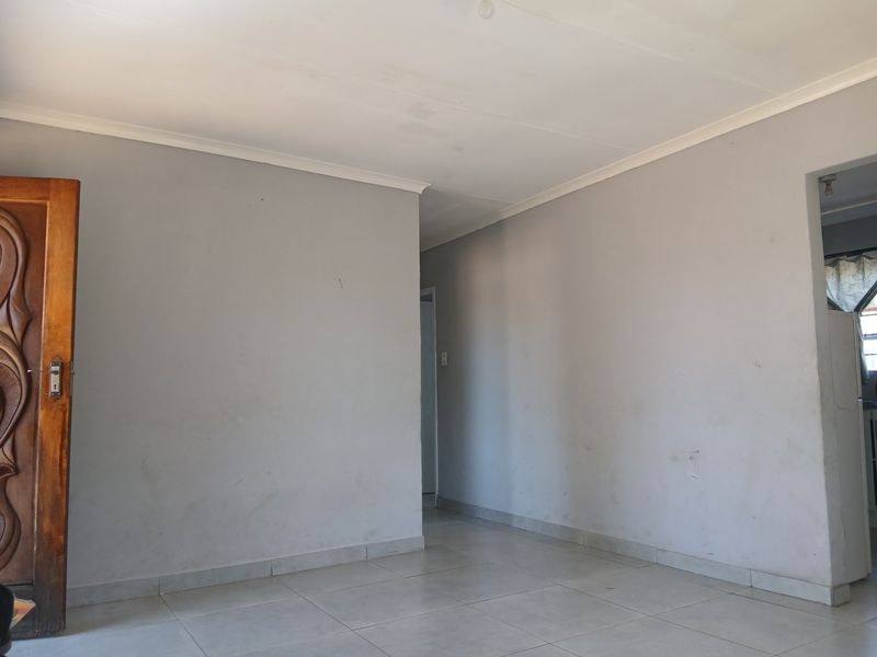 An empty living area featuring neutral tiled flooring, coved ceilings, and a solid wooden door, providing a blank canvas for interior design.