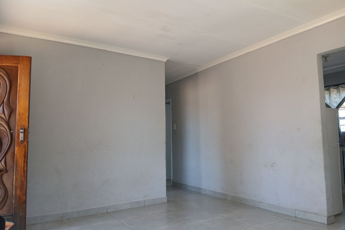 An empty living area featuring neutral tiled flooring, coved ceilings, and a solid wooden door, providing a blank canvas for interior design.