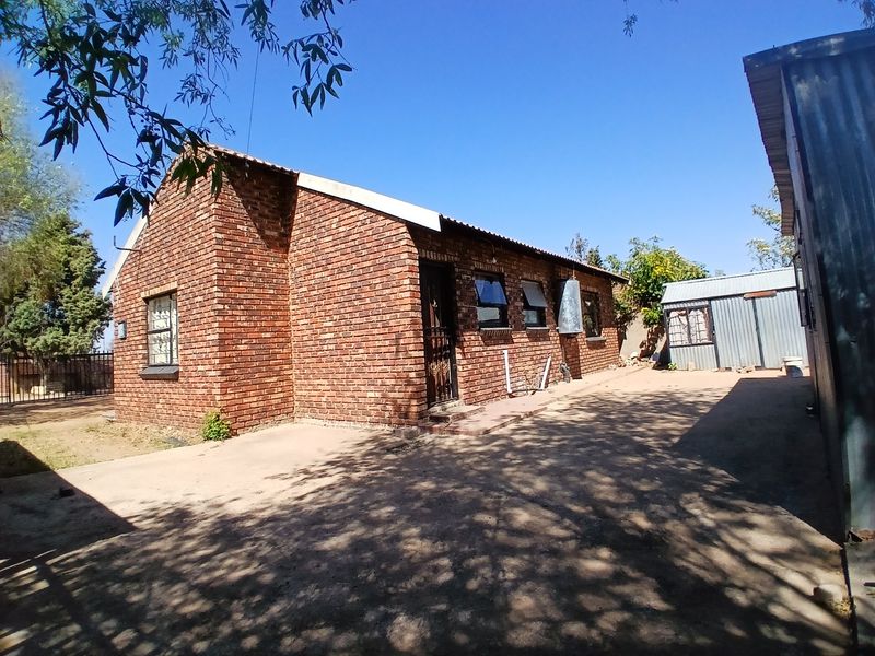 Rear view of a face brick house featuring a corrugated metal roof, security gate, and an adjacent metal outbuilding on a concrete driveway.