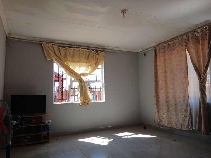 A spacious, empty living room featuring tiled flooring and security bars on the window, offering a blank canvas for potential interior design updates.