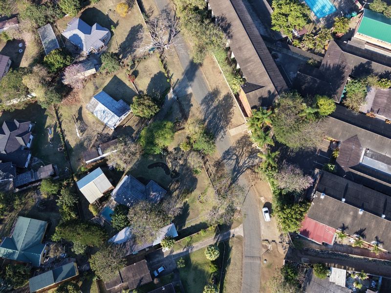 An aerial view of a residential neighborhood showing multiple houses, rooftops, swimming pools, and surrounding garden areas.