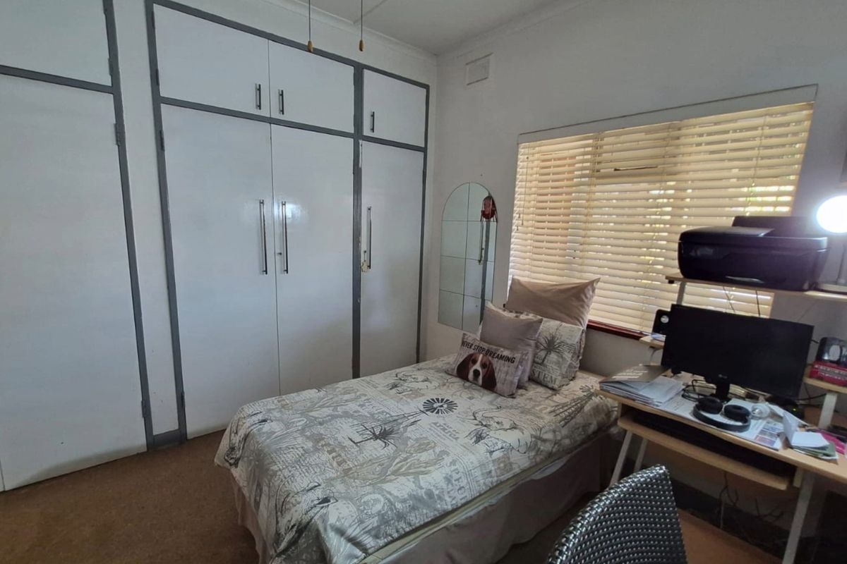 A functional bedroom featuring extensive built-in cupboard storage and venetian blinds, providing a practical space with potential for cosmetic updates.