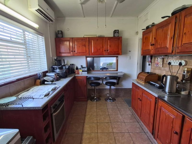 Functional kitchen featuring wooden cabinetry, laminate countertops, built-in oven, tiled backsplash, and a convenient pass-through window to the adjacent living area.