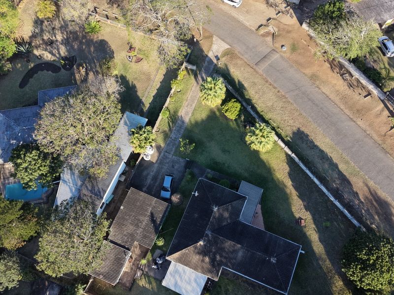 Aerial view of the property showing the main dwelling, tiled roof, swimming pool, driveway, and surrounding garden area.