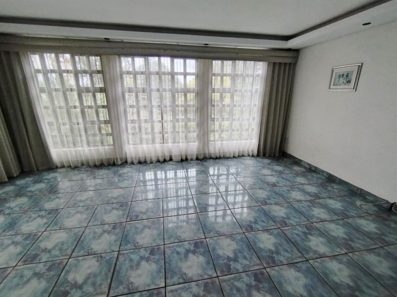An empty living room featuring blue-toned tiled flooring, recessed ceiling lighting, and large grid-pattern windows with integrated curtain tracks.