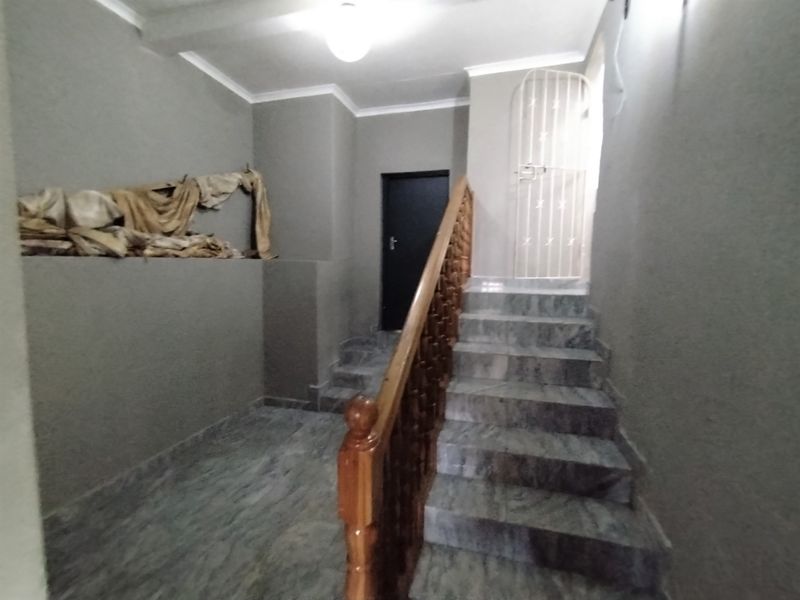 A hallway featuring a marble staircase with a wooden balustrade and a security gate, requiring cosmetic attention to the wall finishes.
