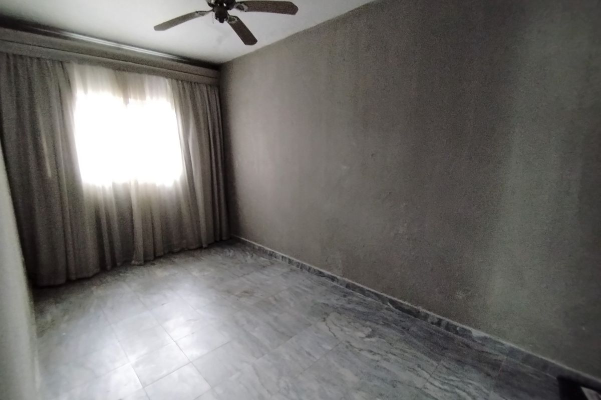 An empty bedroom featuring marble flooring, a ceiling fan, and curtain tracks, showing signs of ceiling water damage and worn wall finishes.