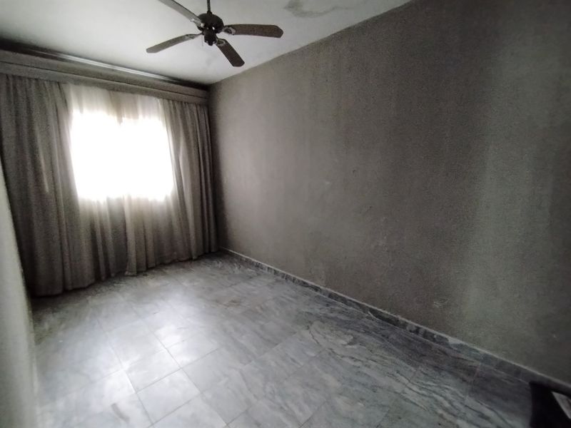 An empty bedroom featuring marble flooring, a ceiling fan, and curtain tracks, showing signs of ceiling water damage and worn wall finishes.